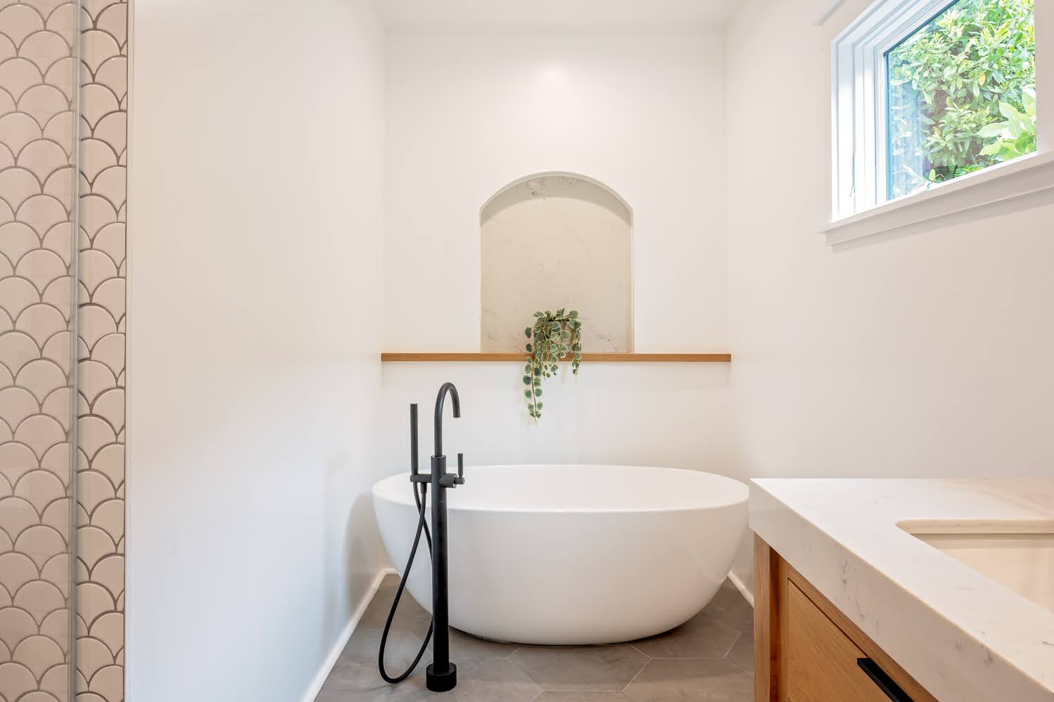 Lillian Master Bathroom — freestanding oval tub with black floor-standing filler beneath an arched niche
