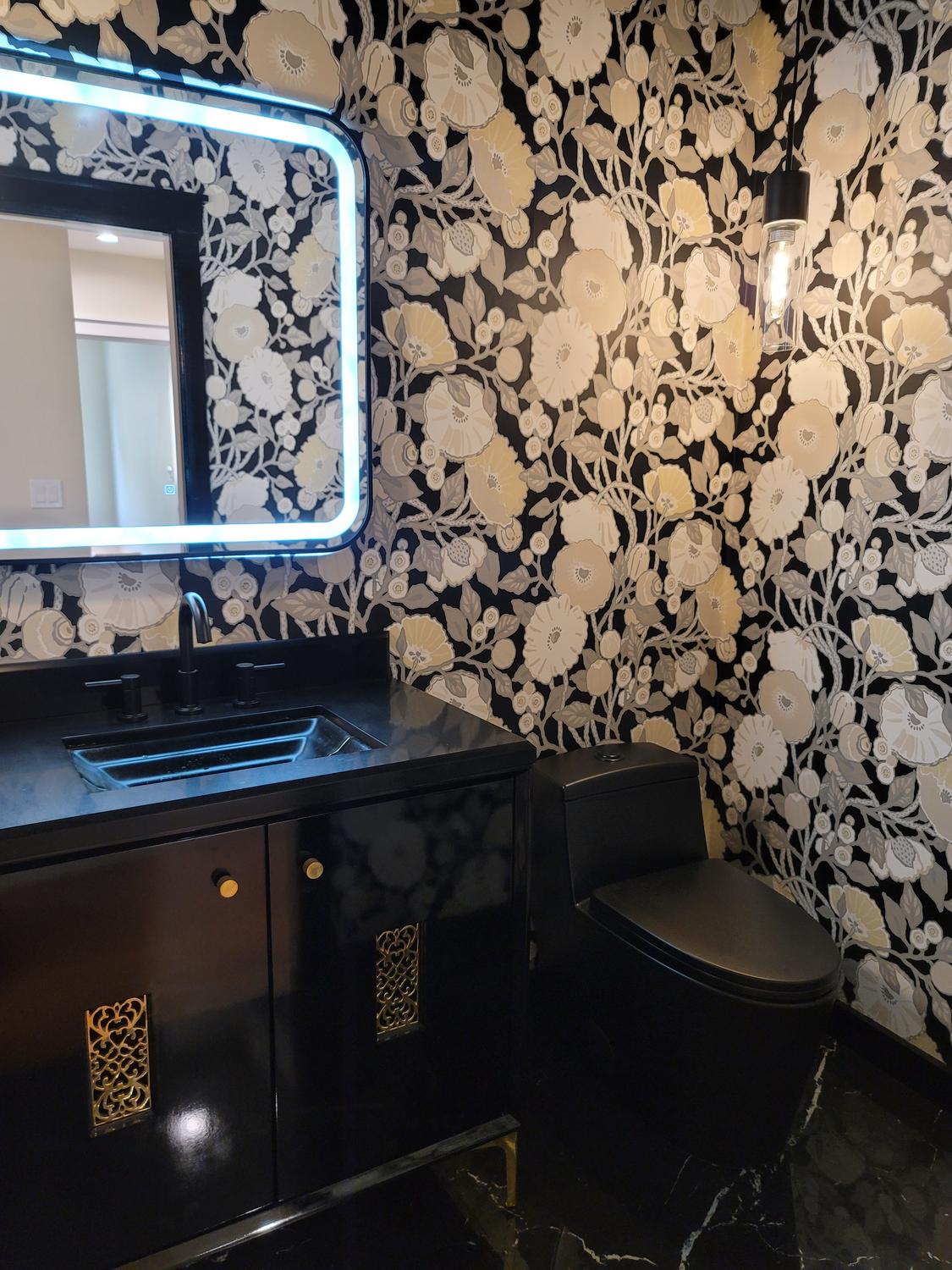 Lillian Powder Room — backlit mirror over the black vanity with gold accents, floral wallpaper and pendant light