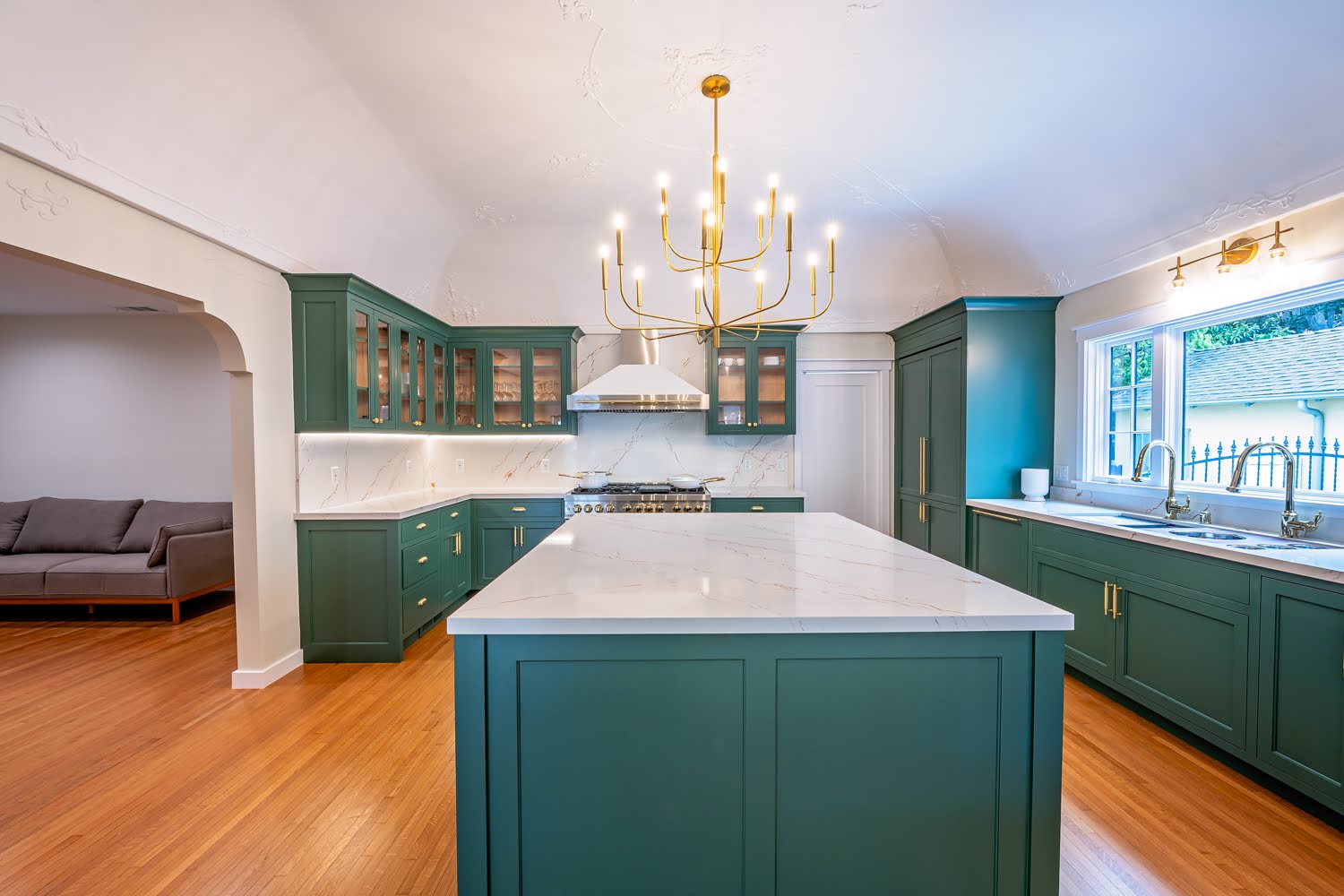 Lillian Kitchen Remodel — wide view of deep green cabinetry, marble island, brass chandelier and hardwood floors